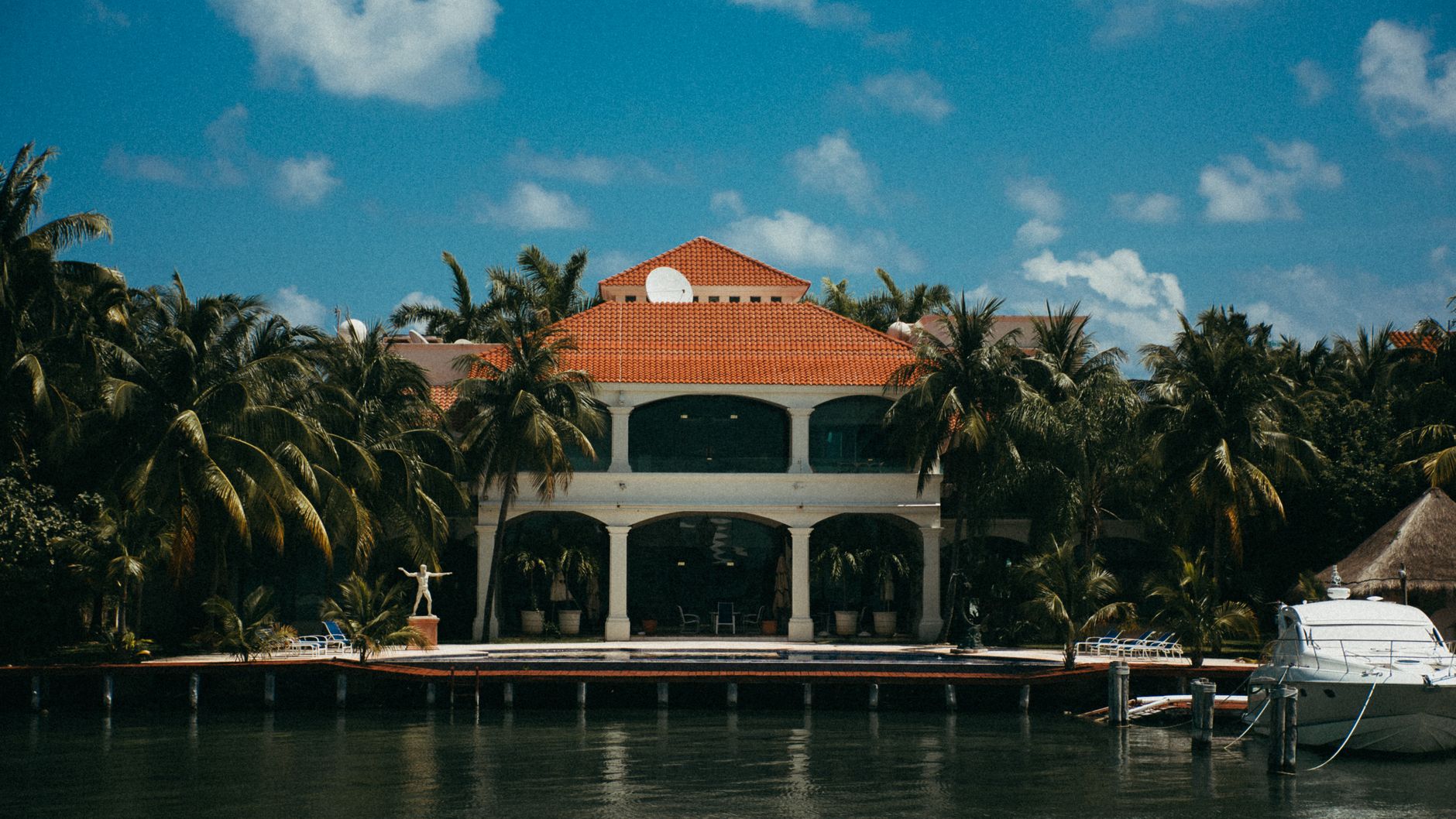Stunning waterfront resort featuring a yacht and palm trees under a bright summer sky.
