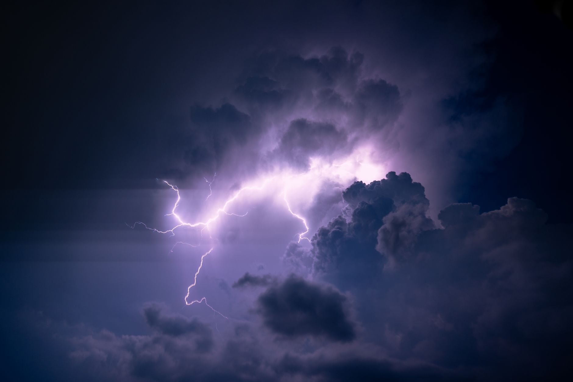A powerful lightning bolt illuminates dark storm clouds, creating a dramatic and moody sky scene.
