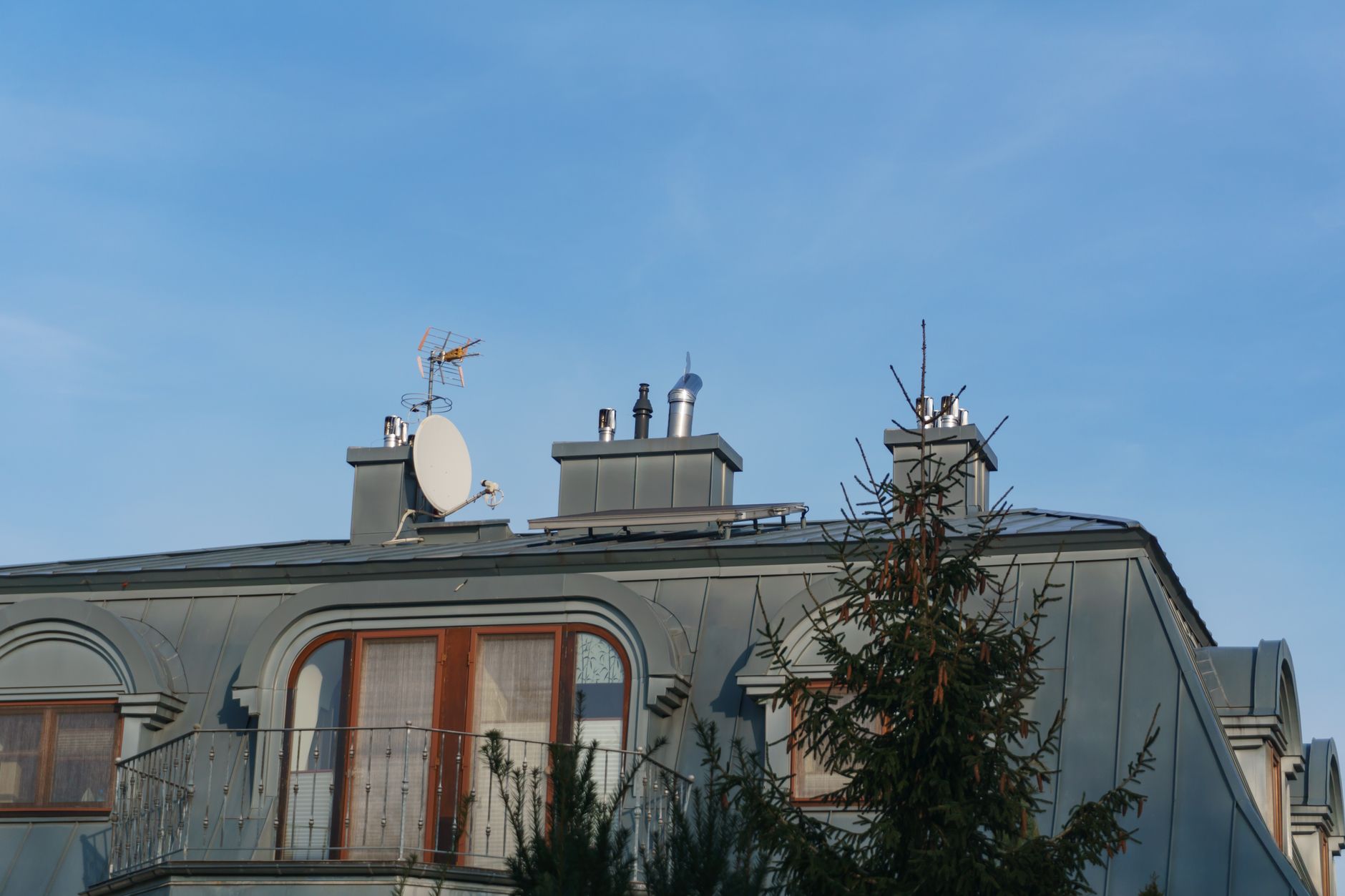 A close-up view of a building roof with antennas and a satellite dish under a clear blue sky.