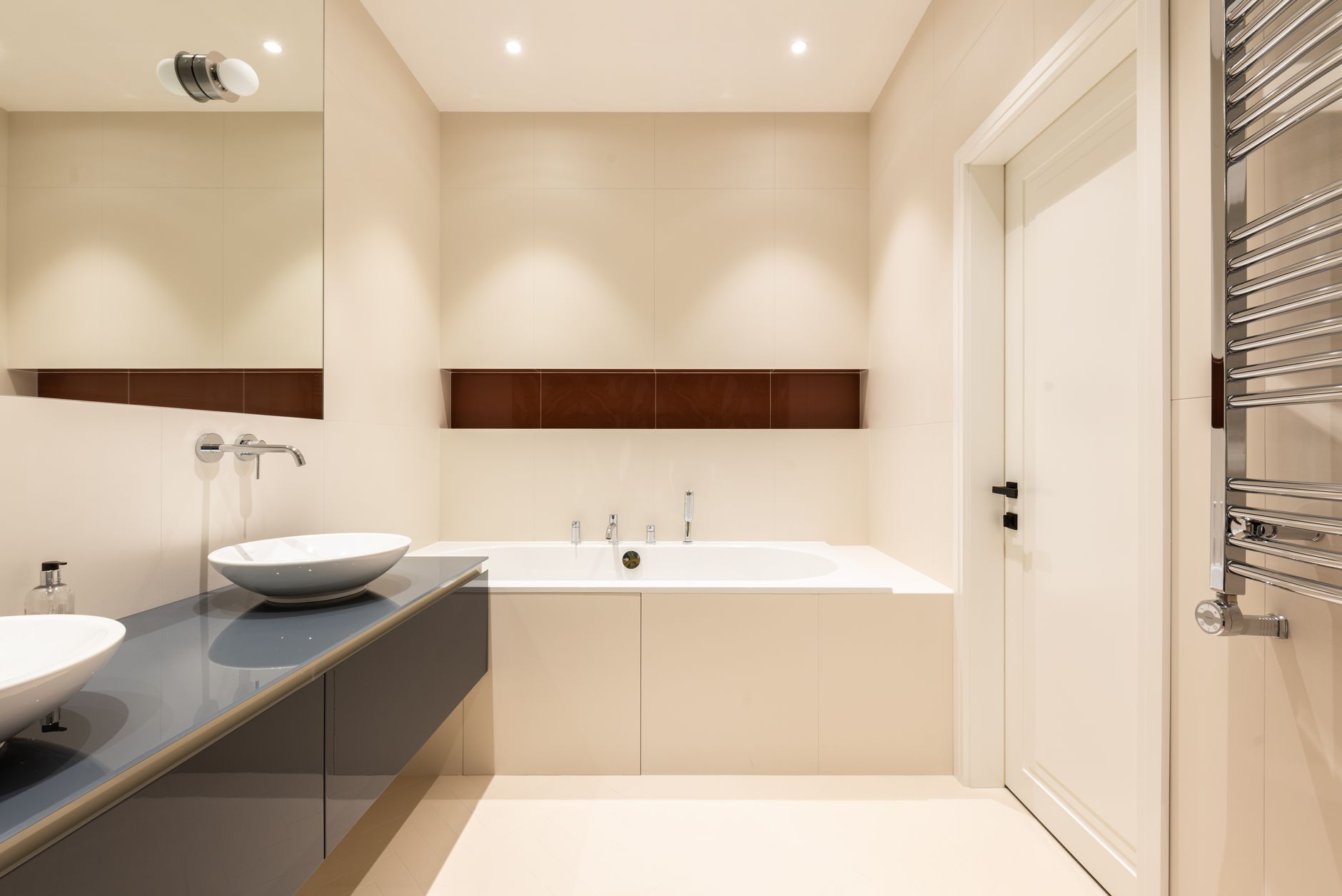 Interior of modern bathroom with sinks on cabinet near tap and mirror near bath and door