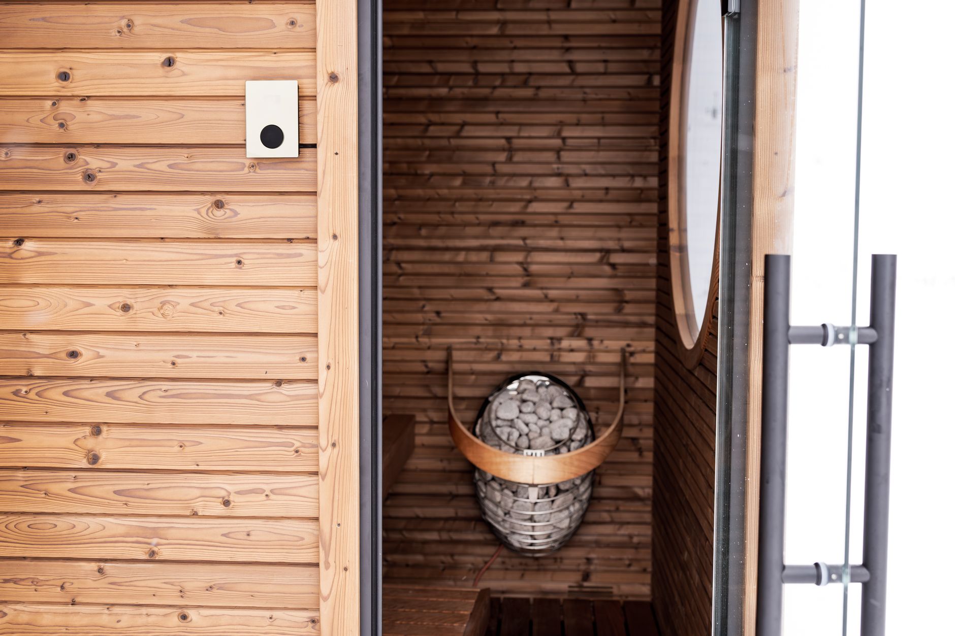 A stylish wooden sauna featuring a modern design with an electric heater and stones, perfect for relaxation.