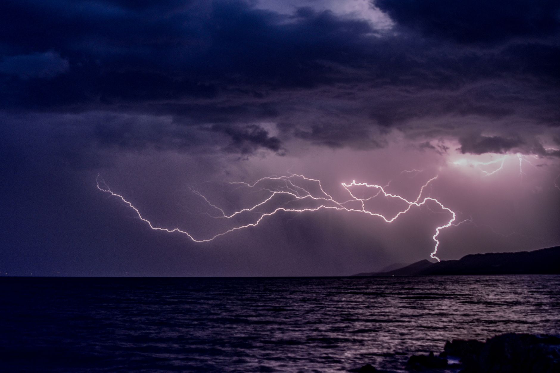 Vivid lightning bolt illuminating dark stormy clouds over a vast ocean, capturing nature's raw power.