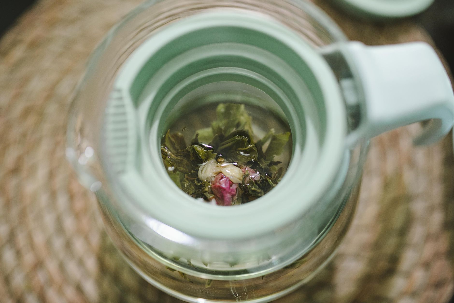 Close-up of a glass teapot with herbal tea and flowers, photographed from above.