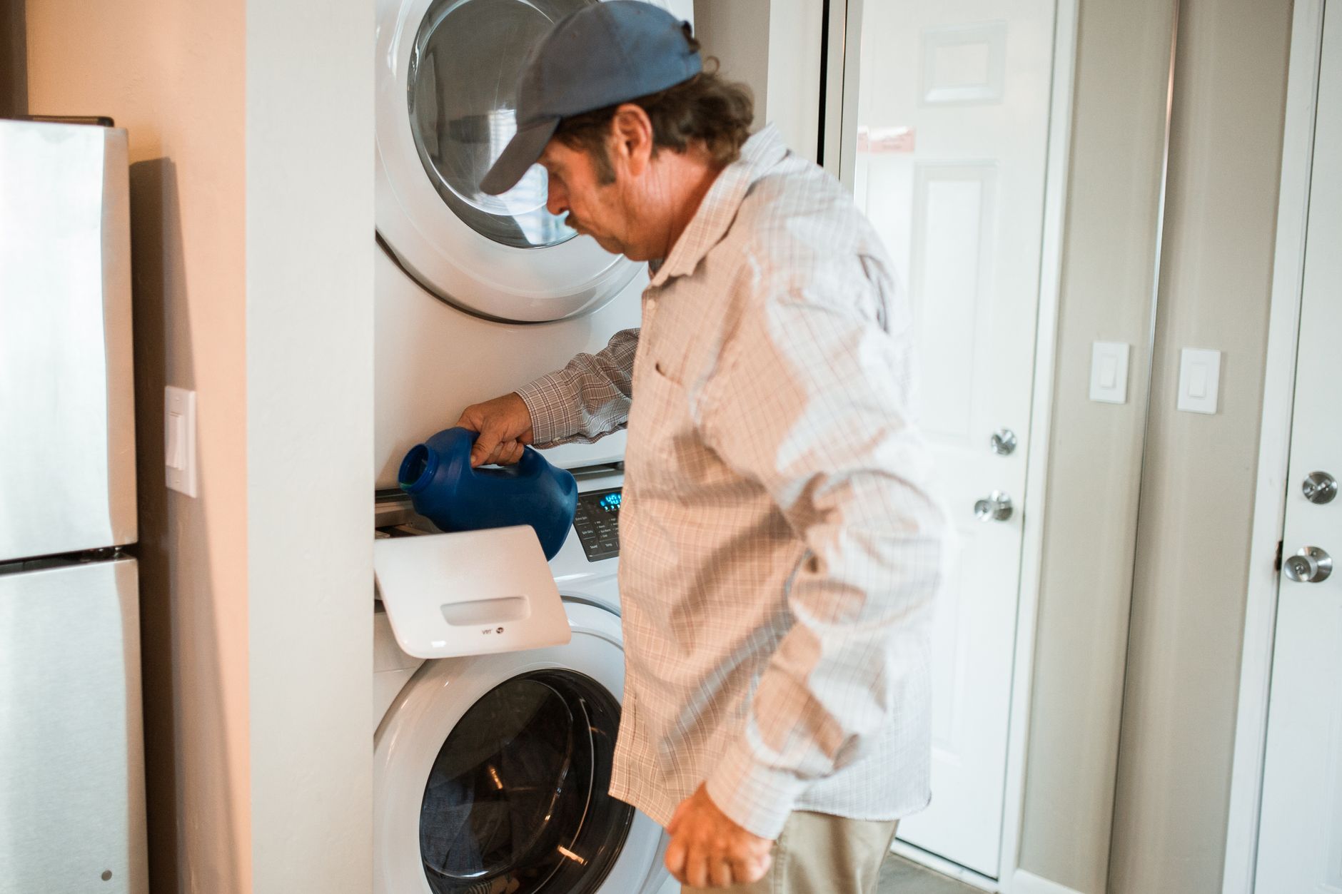 Man pouring liquid detergent into a stacked washer and dryer in a modern laundry room.