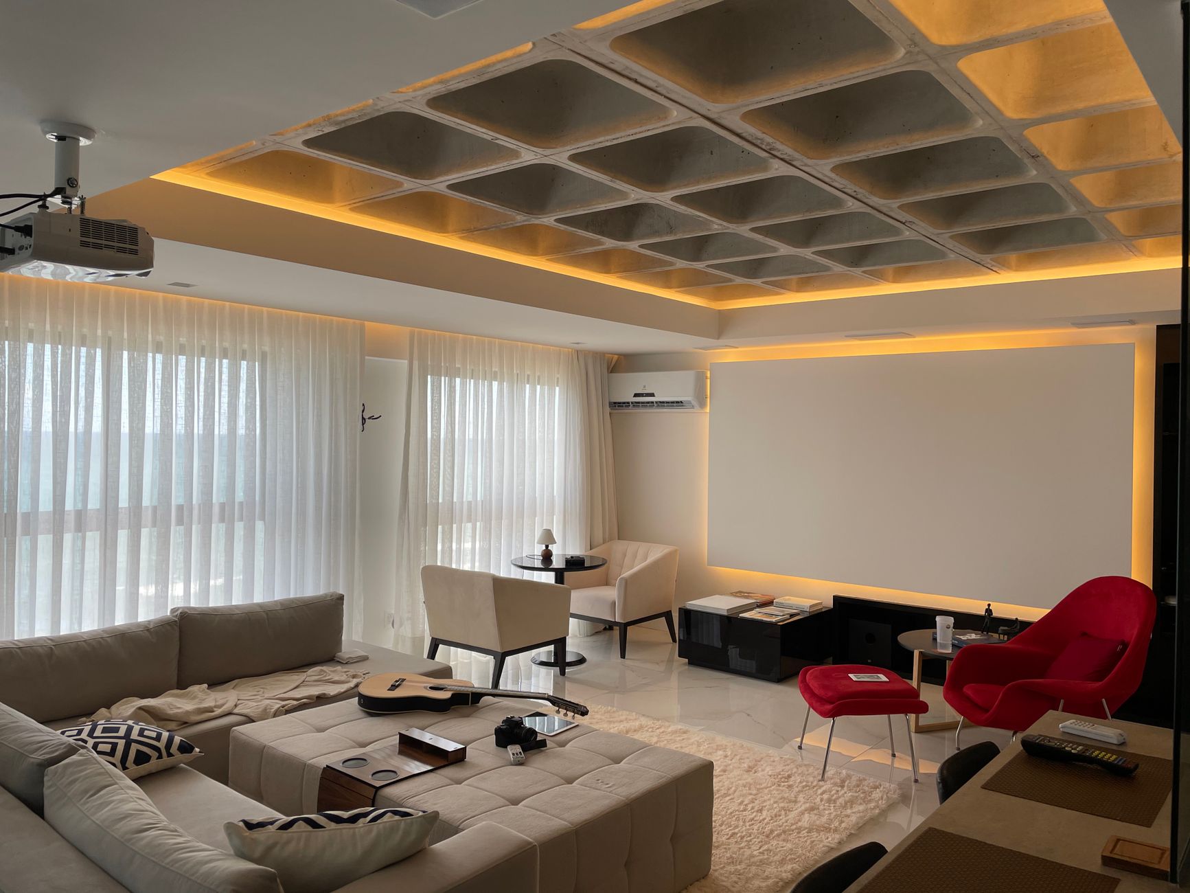 Spacious minimalist living room with natural light, featuring cozy seating and a ceiling projector.