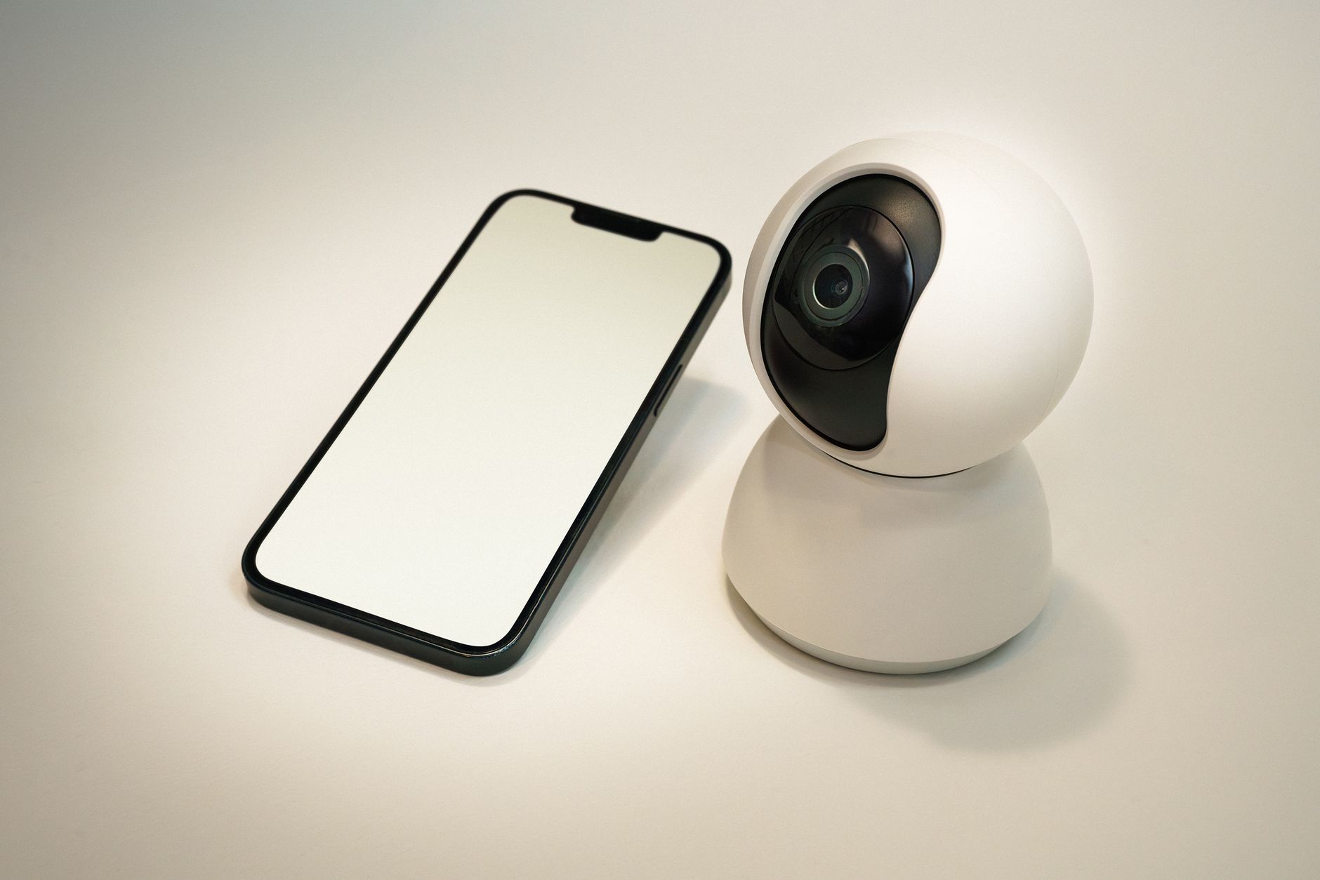 A modern smart home security camera next to a blank screen smartphone, showcasing home automation technology.