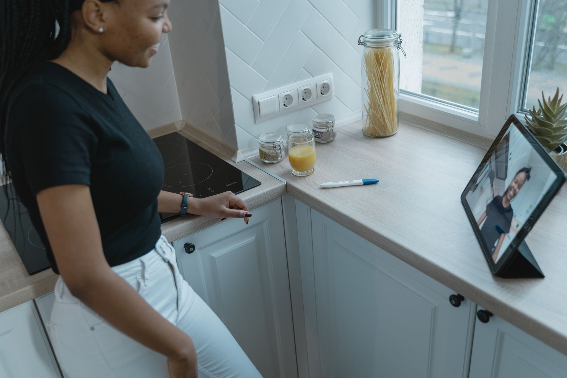 Woman in black top video calling on tablet in a stylish kitchen setting, with decor elements on countertop.