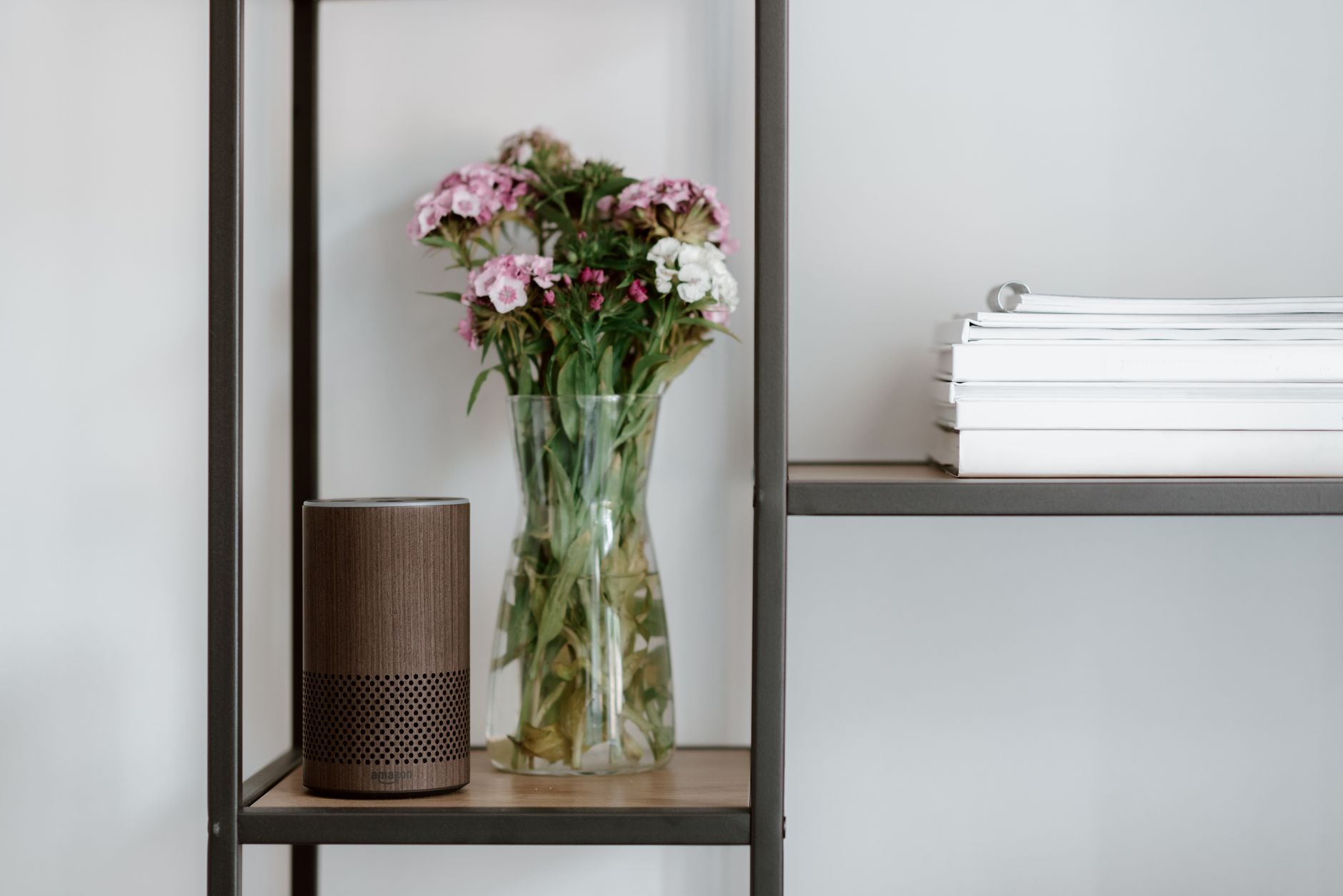 Elegant shelf setup with a smart speaker, vase of flowers, and stacked books for a minimalist touch.