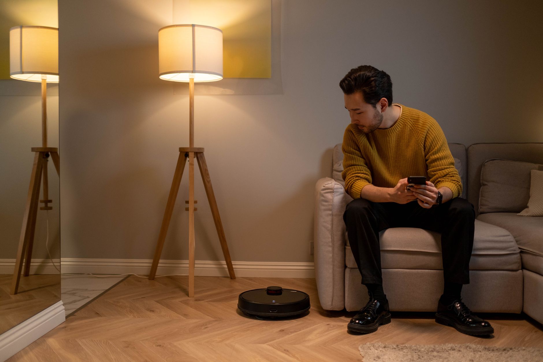 Adult man with a smartphone monitors robot vacuum in a modern living room.