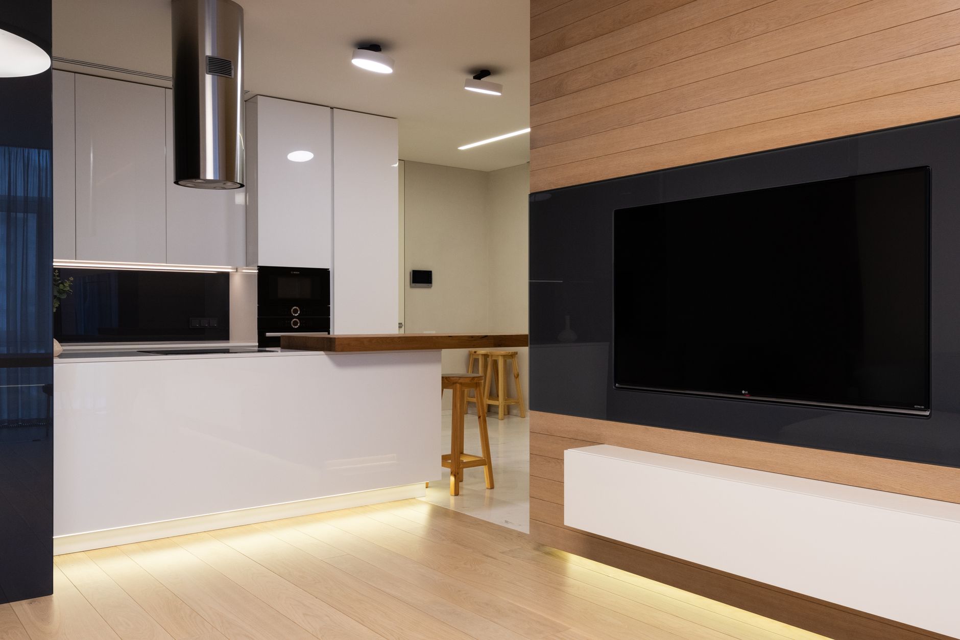 Modern flat with TV set hanging on wall in living room and kitchen furnished with glossy cabinets and shining lamps
