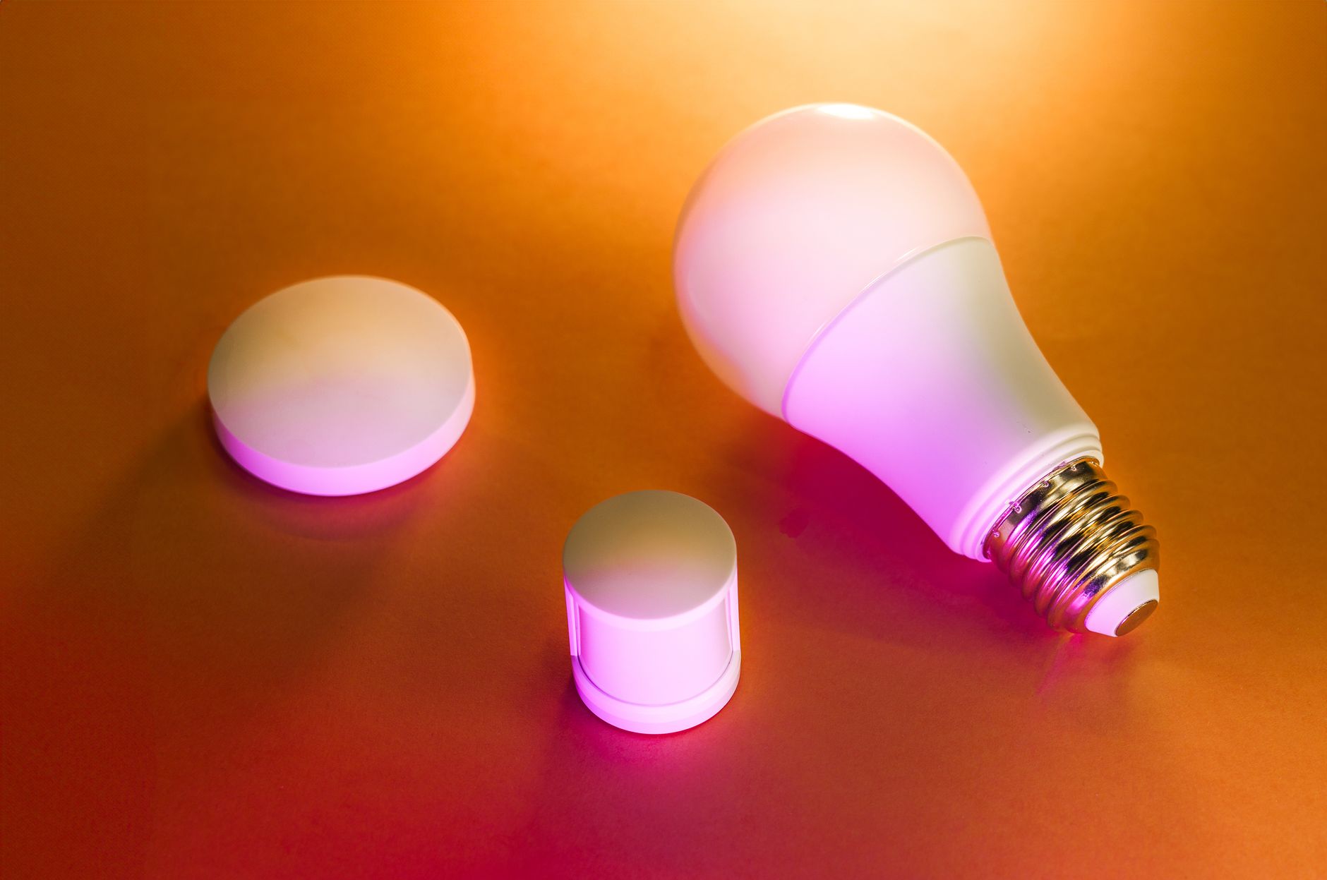 Illuminated LED smart bulb with accessories on a vibrant orange background.