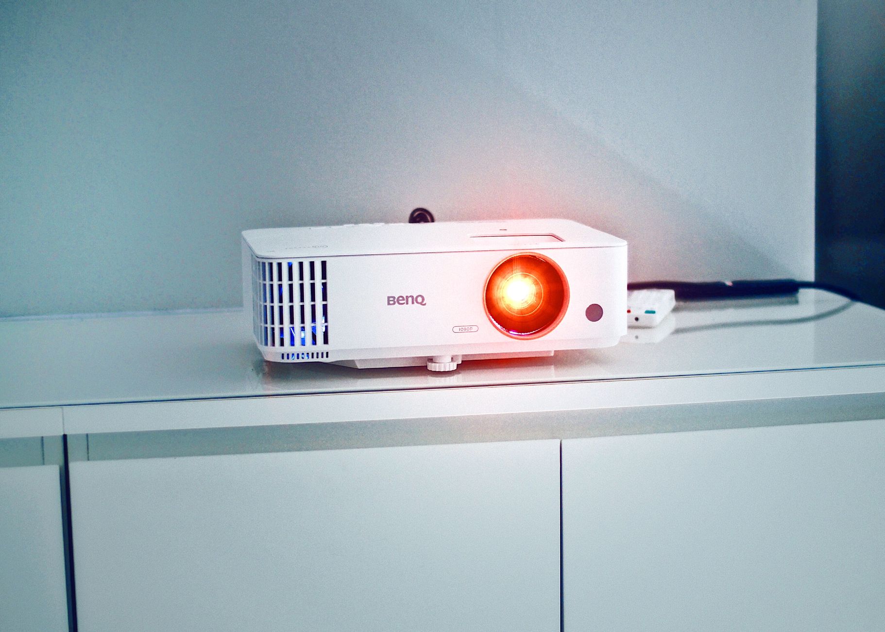 Stylish white projector on a cabinet with glowing lens, perfect for presentations and media rooms.