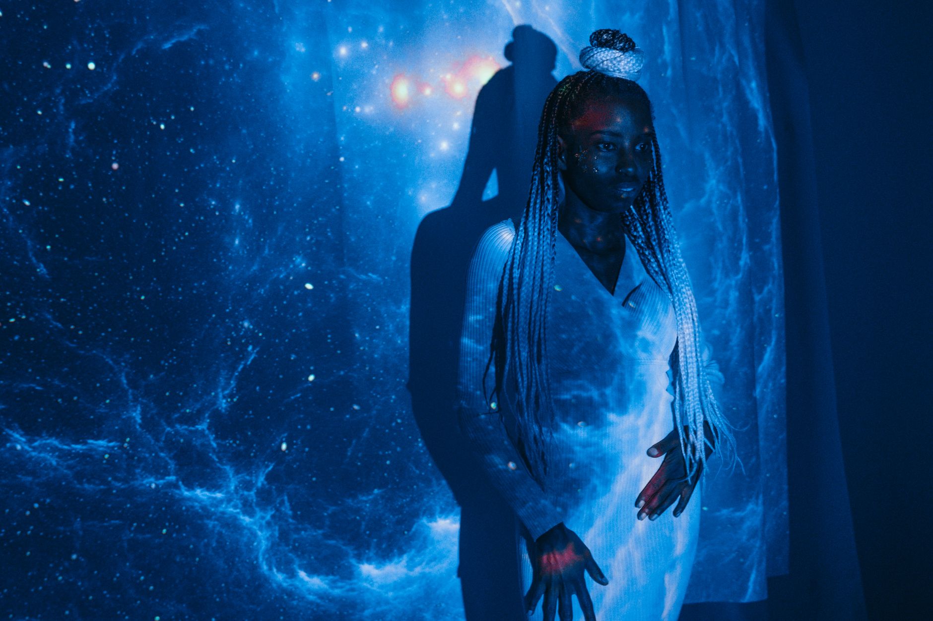 A woman poses with galaxy projections on her, creating a cosmic art vibe.
