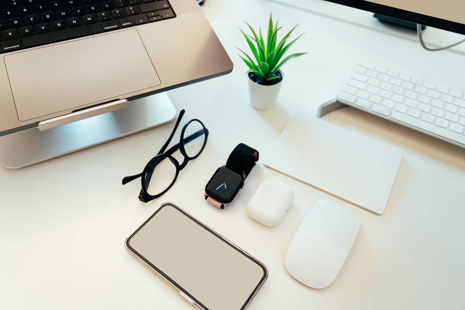 Overhead view of a sleek workspace with a laptop, smartphone, smartwatch, and tech accessories.