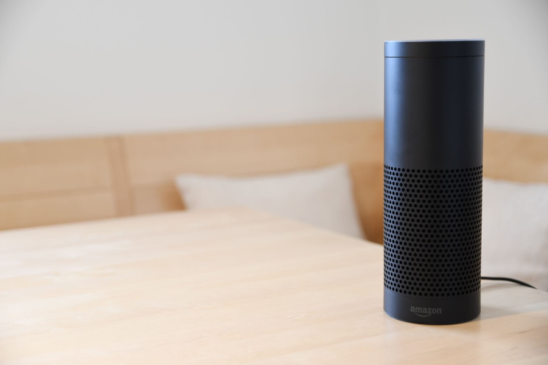 A black smart speaker resting on a light-colored wooden table in a cozy indoor setting.