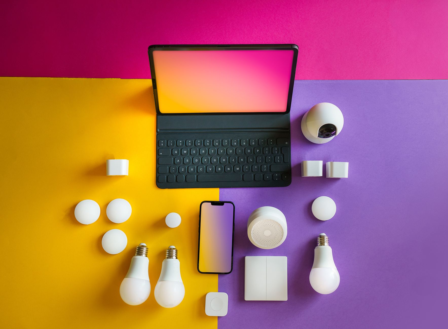Flat lay of smart home devices including a tablet, smartphone, and bulbs on a vibrant background.