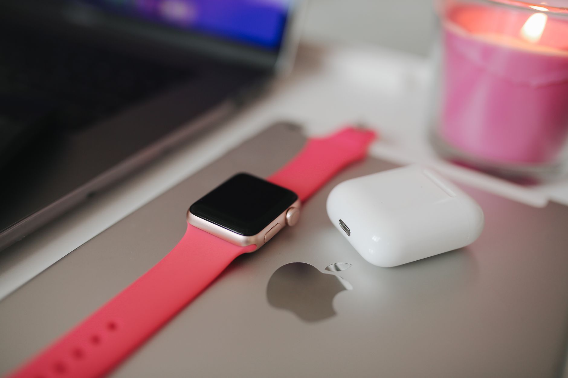 Close-up of modern tech gadgets including a smartwatch, earbuds, and a laptop on a stylish desk.