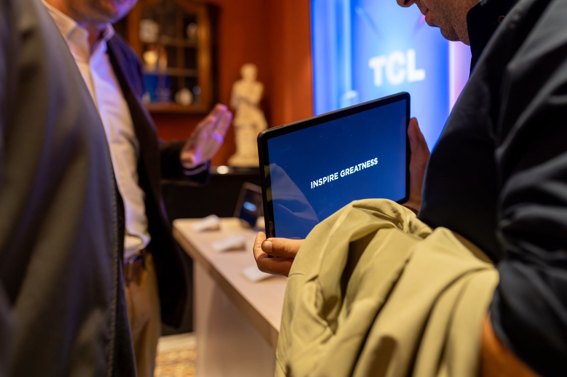 A man holding a tablet with 'Inspire Greatness' displayed at a tech event indoors.