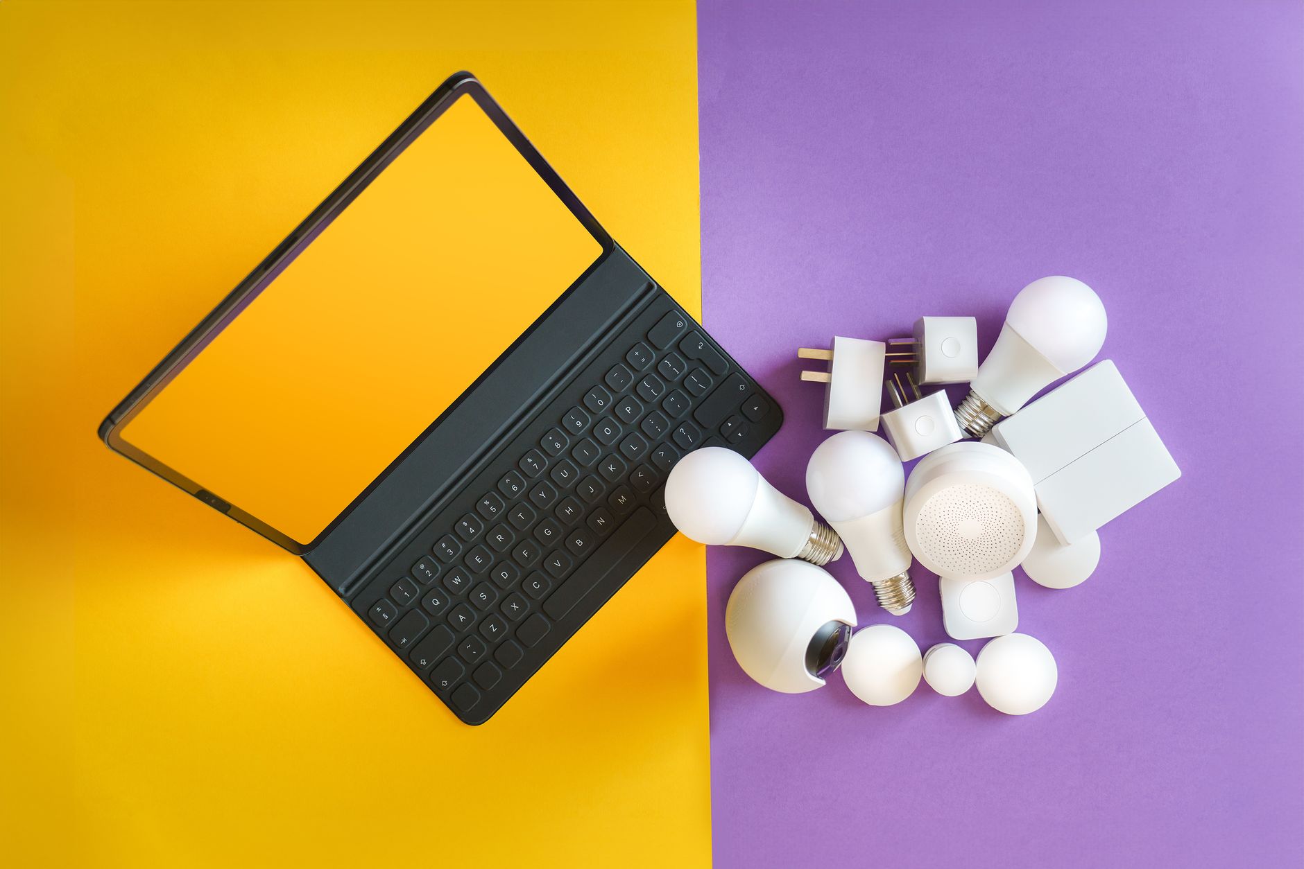 Flat lay of smart home gadgets and a keyboard on vibrant background depicting modern technology.