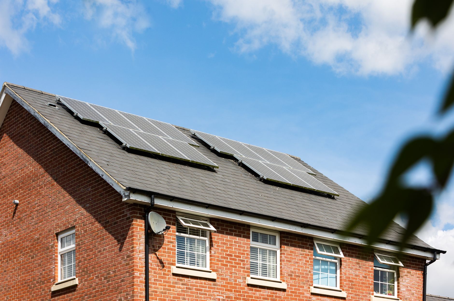 Brick house featuring solar panels on the roof under a clear blue sky, promoting sustainable energy.