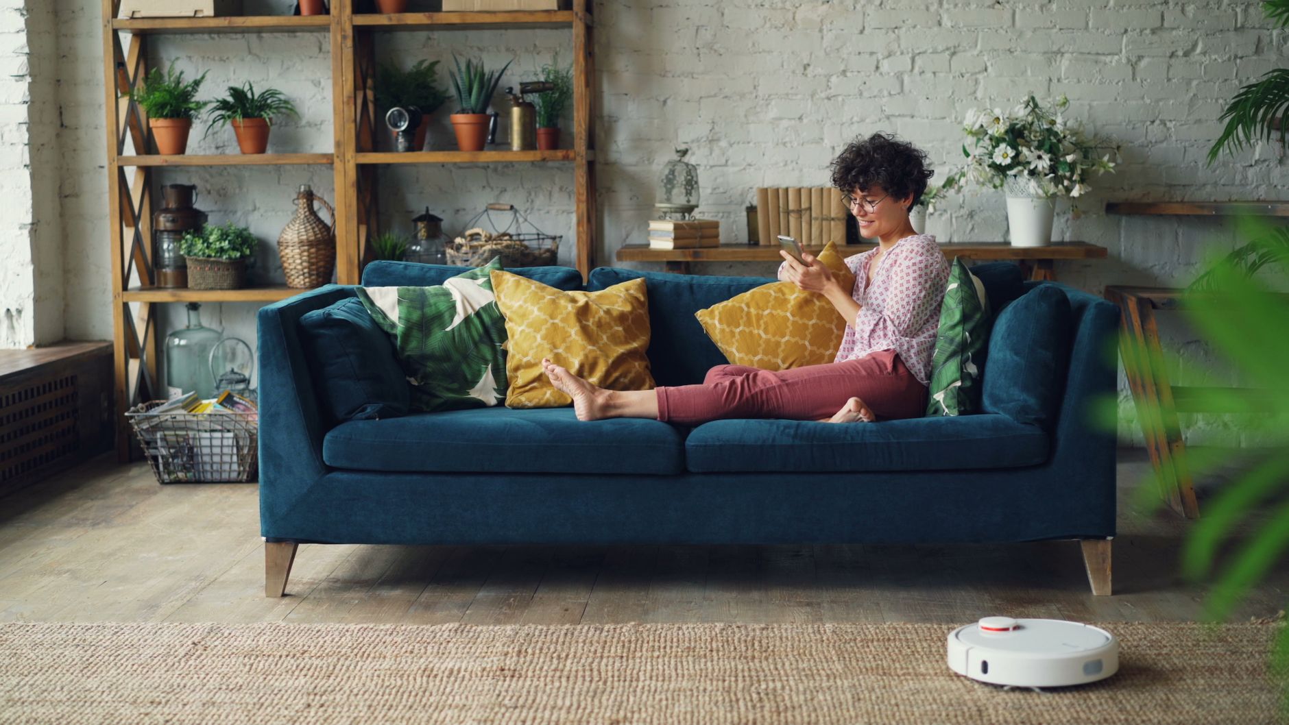 Adult enjoying a relaxing day on a cozy sofa with a phone and smart cleaning robot.