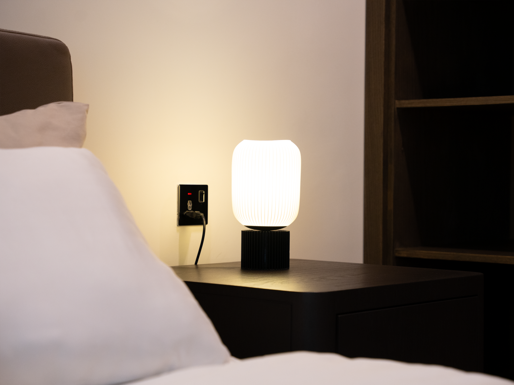 A minimalist bedside lamp illuminates a modern bedroom setting, highlighting comfort and elegance.
