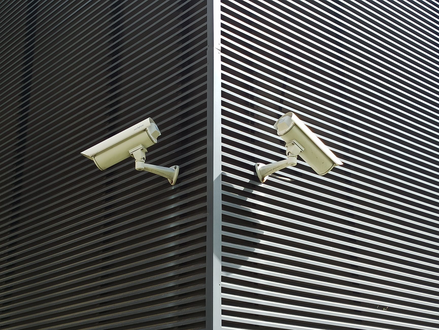 Two security cameras mounted on a slatted wall for surveillance.